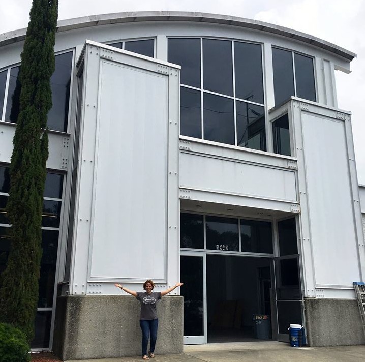 Beau's Coffee owner Amy Wright stands ant-like in front of the massive former Hummer building on New Centre Drive. Beau's will relocate to the 5,000 square foot site next month. Courtesy photo.