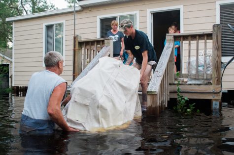 Mike Hicks, left, helps lift his grill onto his back porch in a flooded neighborhood on Alexis Hales Road near the Black River in Currie, North Carolina on Wednesday evening, September 19, 2018. (Port City Daily photo | Mark Darrough)