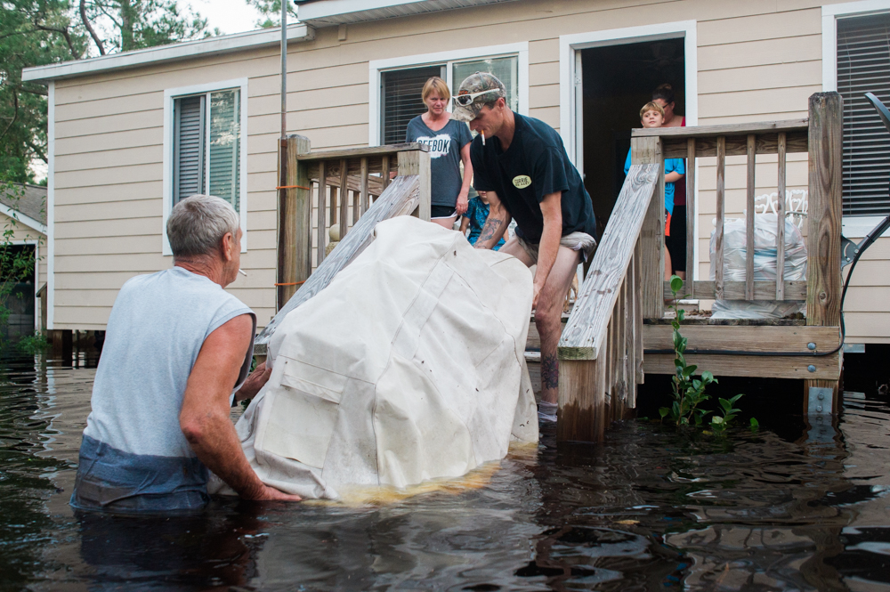 Mike Hicks, left, helps lift his grill onto his back porch in a flooded neighborhood on Alexis Hales Road near the Black River in Currie, North Carolina on Wednesday evening, September 19, 2018. (Port City Daily photo | Mark Darrough)
