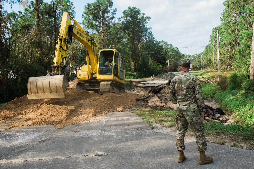 First Sergeant Andrew McNulty oversees a contracted excavator filling in a washout on Boiling Springs Lake Road in the town of Boiling Springs Lake. (Port City Daily photo | Mark Darrough)