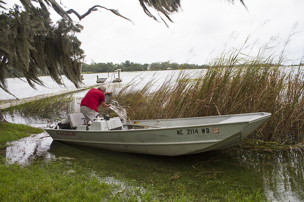 A boat owner on Hewletts Creek transfers water out of his vessel after it became dislodged from heavy winds Thursday afternoon. (Port City Daily/Johanna Ferebee)