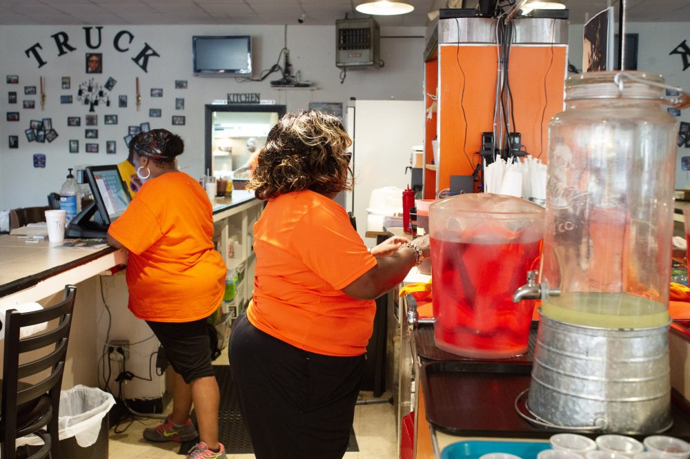 Mama Rona, right, works behind the counter; a photo shrine for her recently passed brother is seen on the back wall behind her. (Port City Daily photo/Mark Darrough)