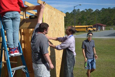 Hugh Hirth assists Carpentry I students build a permitted, stick-built playhouse which will be auctioned off at the end of the school year. (Port City Daily photo/Courtesy Brunswick County Schools)