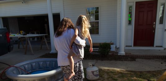 Daphene Morris and her five-year-old daughter Elizabeth walk through her neighbor's yard, where people are still living in a FEMA trailer, eight months after Hurricane Florence. (Port City Daily photo/Johanna Ferebee)