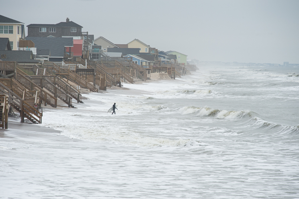 A man walks out in the high tide to surf just north of the Surf City Ocean Pier late Monday morning (Port City Daily photo/Mark Darrough)