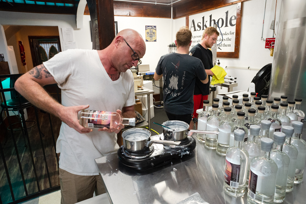 Mason Inlet Distillery owner Tom Curran dips a bottle of his Go Bananas brandy into hot wax for a sealed top. (Port City Daily photo/Mark Darrough)