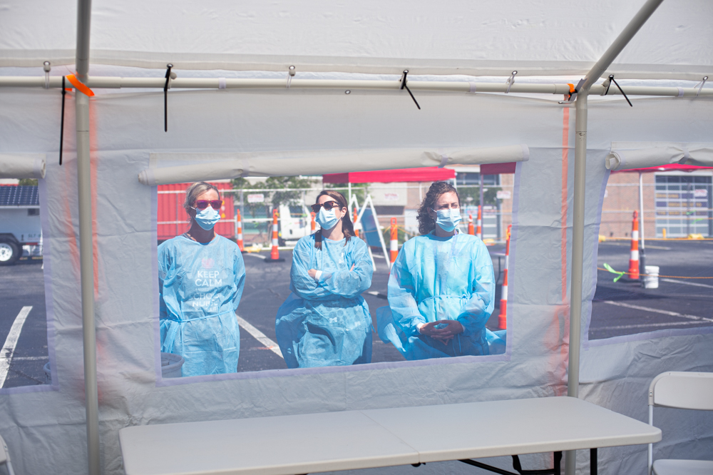 Public health nurses stand outside a drive-through tent where they will be administering nasal swabs for New Hanover County residents experiencing symptoms of Covid-19. (Port City Daily photo/Mark Darrough)