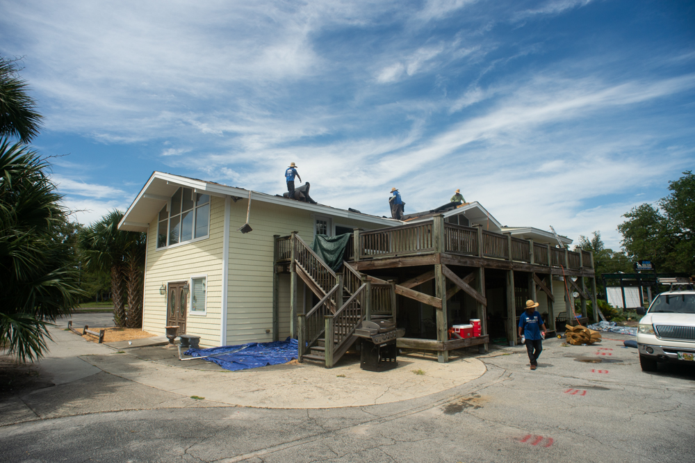 A construction crew removes the underlying tar paper on the clubhouse roof before installing new shingles. (Port City Daily photo/Mark Darrough)